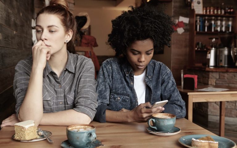 Billede af to kvinder på en café. Den ene er opslugt i sin telefon.