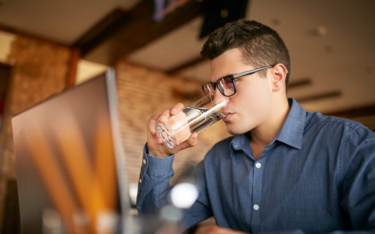Person med briller tager en slurk af sit glas vand.