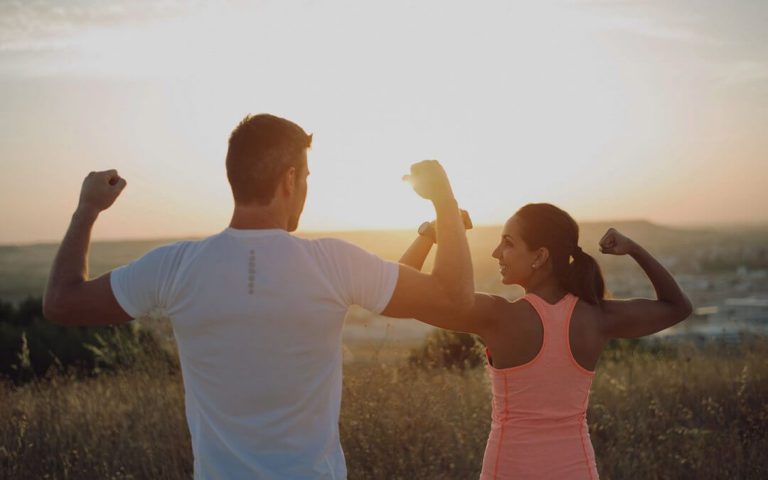 Billede af en mand og en kvinde der flexer deres muskler foran en solnedgang.